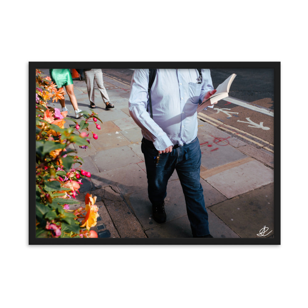 Photographie 'La Marche' par Ilan Shoham, représentant un homme en chemise bleue marchant paisiblement et lisant un livre dans les rues animées de Londres, symbolisant la sérénité et la résistance au milieu du tumulte urbain, tout en apportant une tranquillité visuelle à votre espace de vie ou de travail.