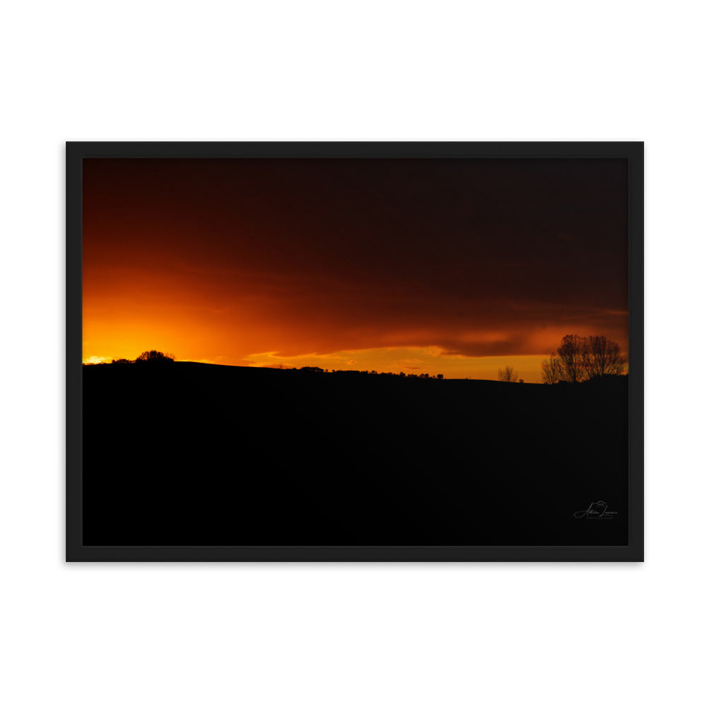 Photographie d'un coucher de soleil flamboyant, par Adrien Louraco, illustrant un ciel vibrant de teintes ardentes contre une silhouette de campagne.