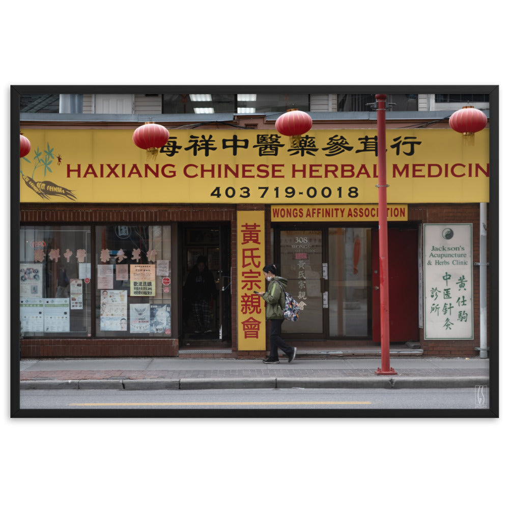 Photographie de rue à Calgary montrant une femme avec un masque abaissé devant une boutique d'herbes médicinales chinoises, capturée par Galdric Sibiude, reflétant le quotidien urbain.