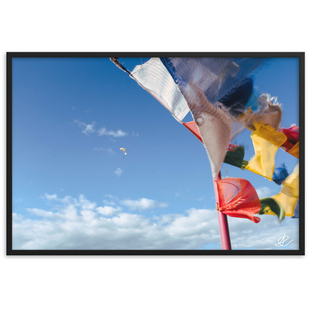 Photographie capturant des drapeaux colorés ondulant au vent et un parapente dans un ciel bleu, par Ilan Shoham, symbolisant la joie et l'esprit d'aventure.