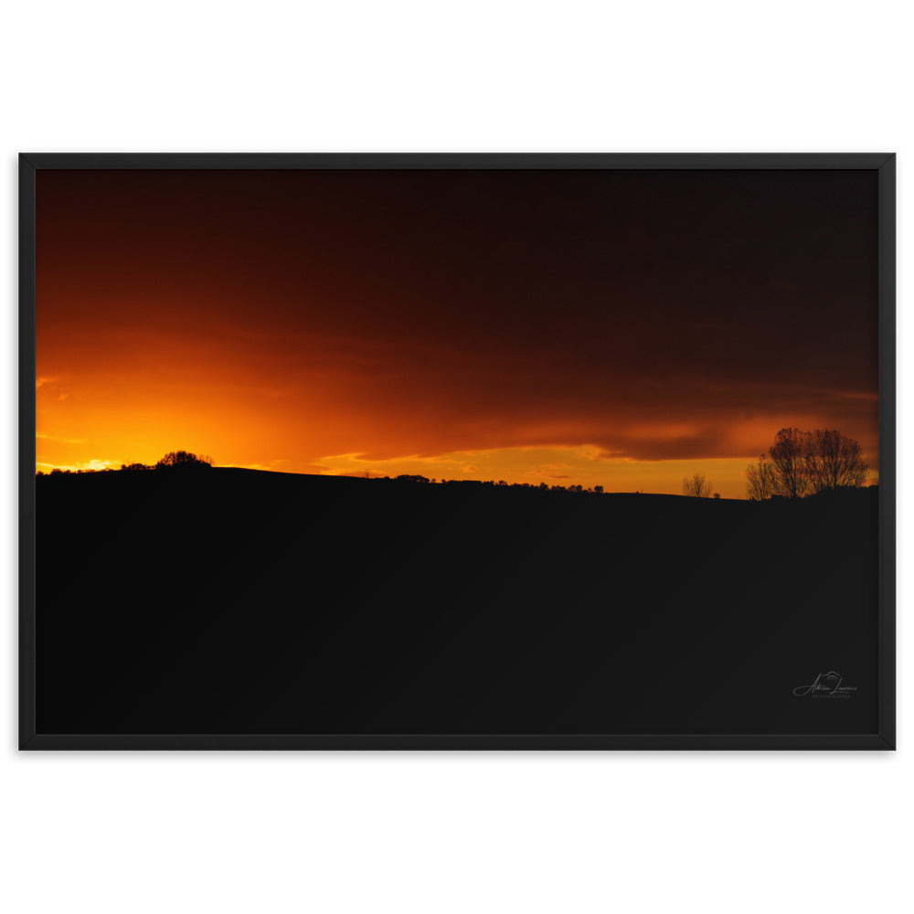 Photographie d'un coucher de soleil flamboyant, par Adrien Louraco, illustrant un ciel vibrant de teintes ardentes contre une silhouette de campagne.