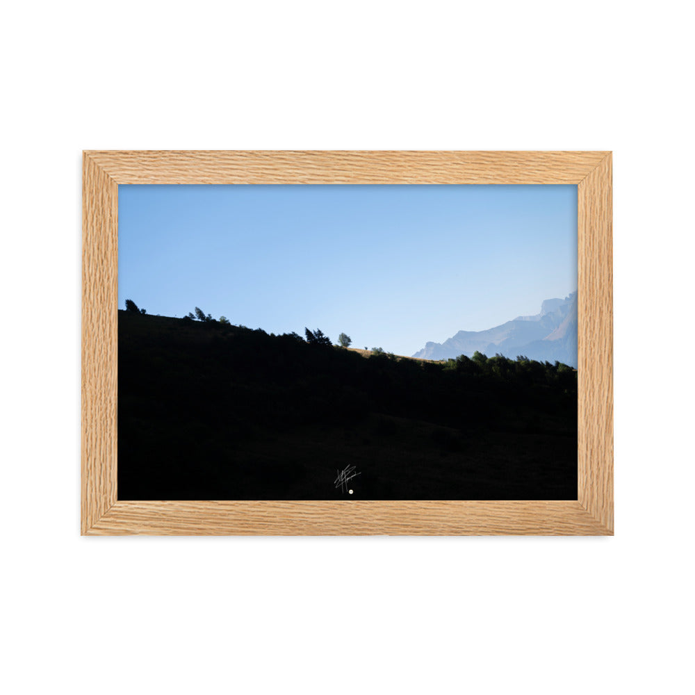 Poster encadré 'Le Tournis', mettant en scène un arbre solitaire éclairé par le soleil sur un flanc de montagne sombre, capturant l'essence du mystère et de la lumière alpine.