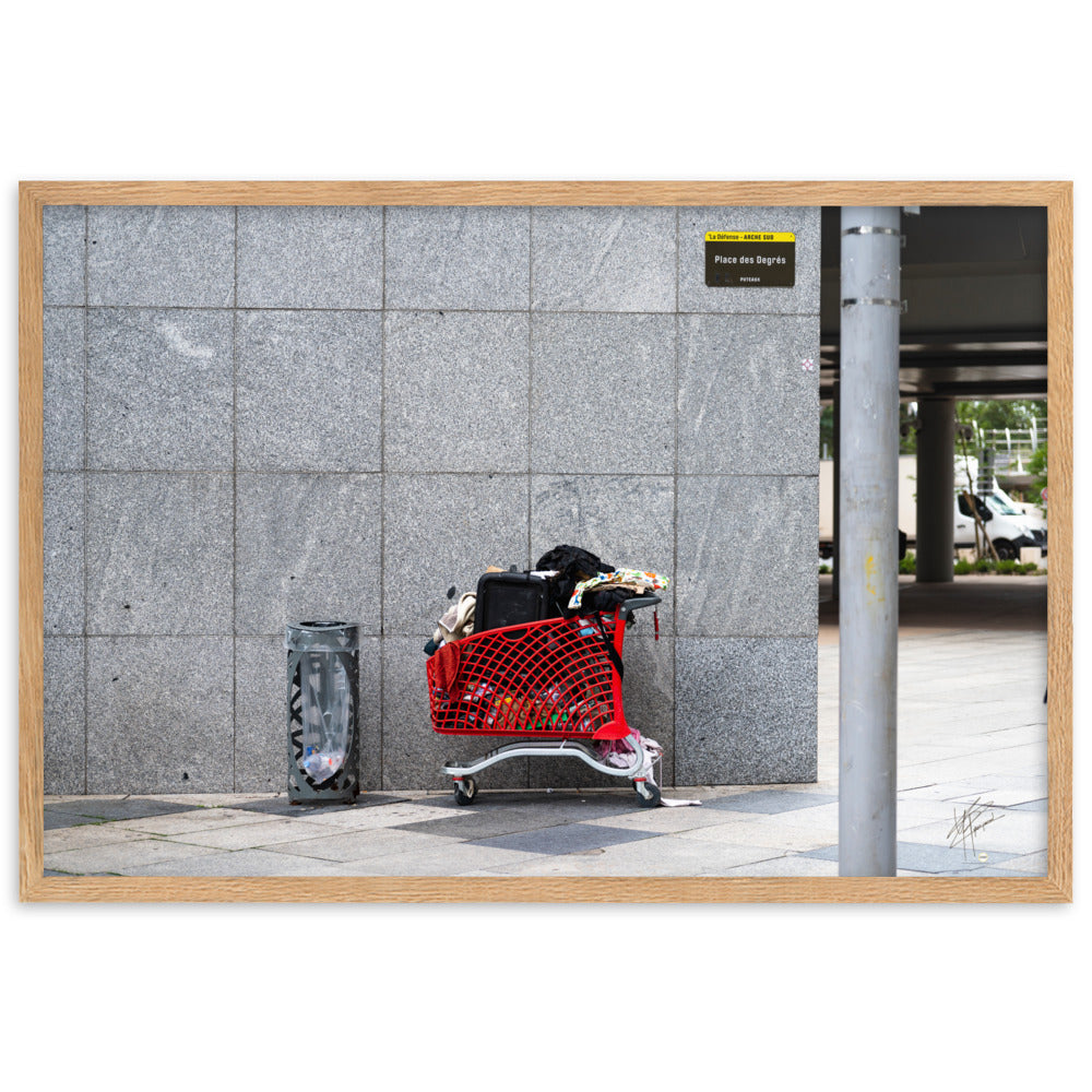 Photographie d'un caddie rouge abandonné à La Défense, juxtaposé à une poubelle, évoquant une méditation sur la consommation et l'abandon dans un contexte urbain moderne.