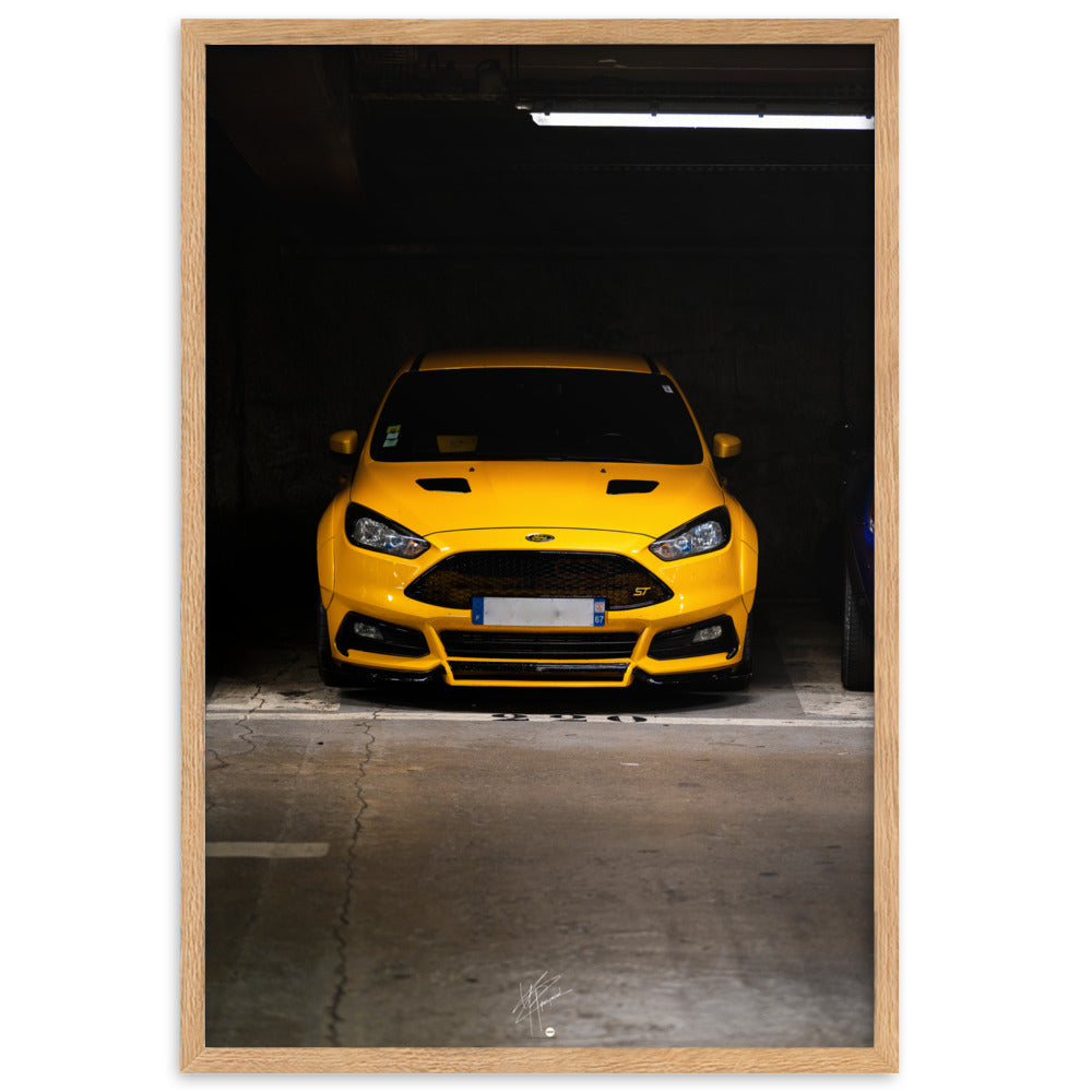 Vue frontale d'une Ford Focus ST en éclatant jaune, mise en lumière dans un parking souterrain avec un éclairage distinctif, encadrement en chêne.