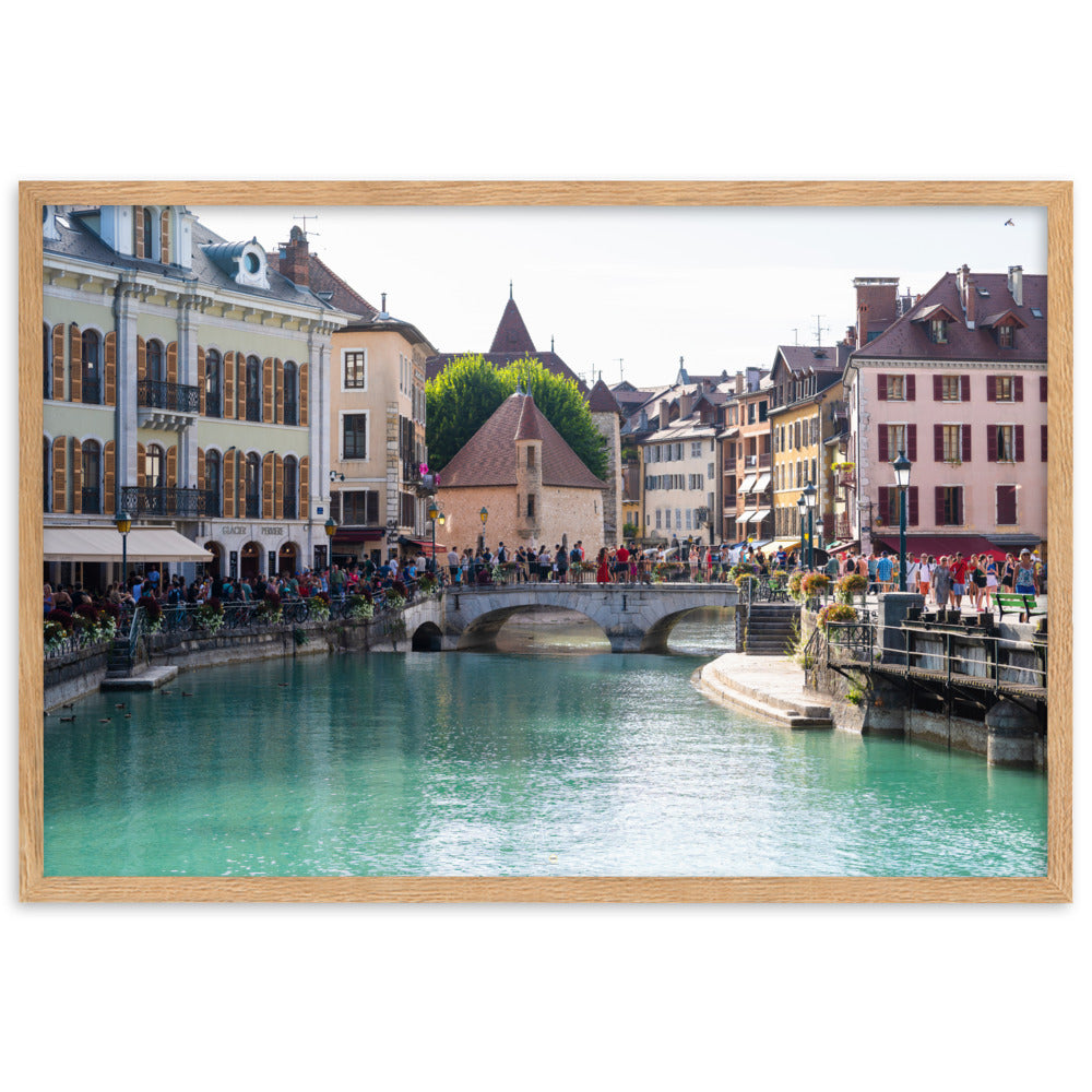 Vue estivale d'Annecy, mettant en lumière le Pont Perrière et le Palais de l'Île, encadrée d'un bois de chêne.