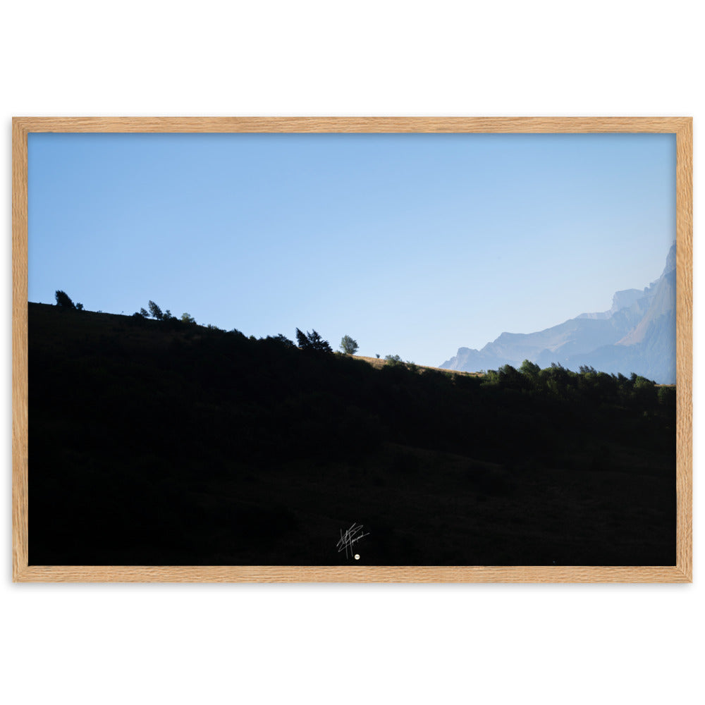 Poster encadré 'Le Tournis', mettant en scène un arbre solitaire éclairé par le soleil sur un flanc de montagne sombre, capturant l'essence du mystère et de la lumière alpine.