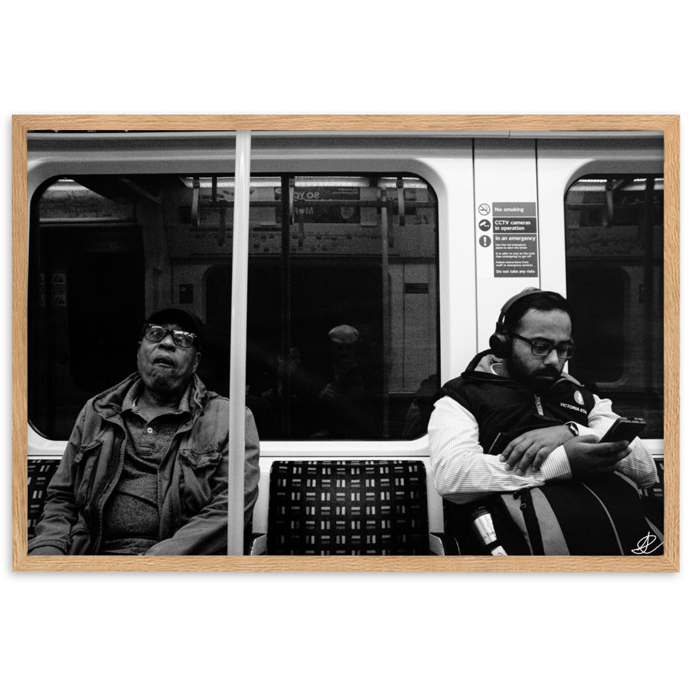 Poster encadré 'Fin de journée' en noir et blanc par Ilan Shoham, capturant une scène paisible du métro londonien avec un siège vide encadré par deux individus assis, symbolisant les distances sociales dans l'agitation urbaine.