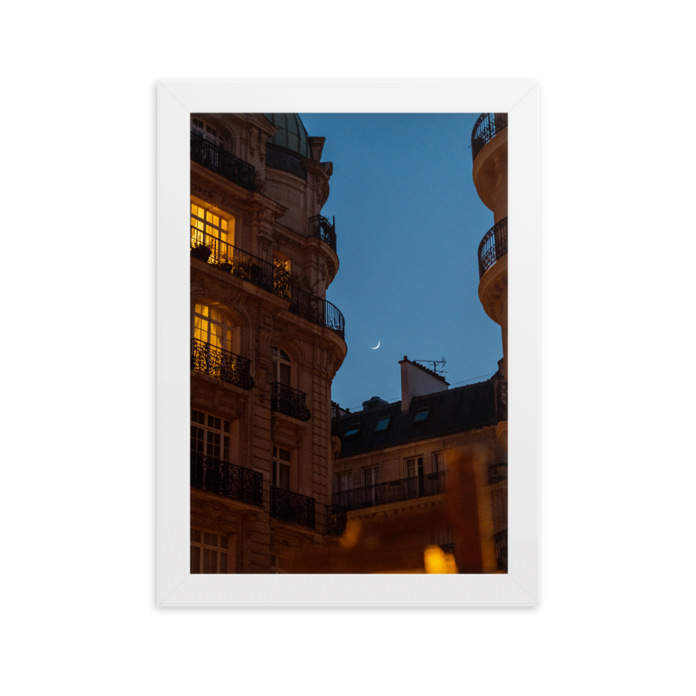 Croissant de lune entre des immeubles haussmanniens éclairés la nuit.