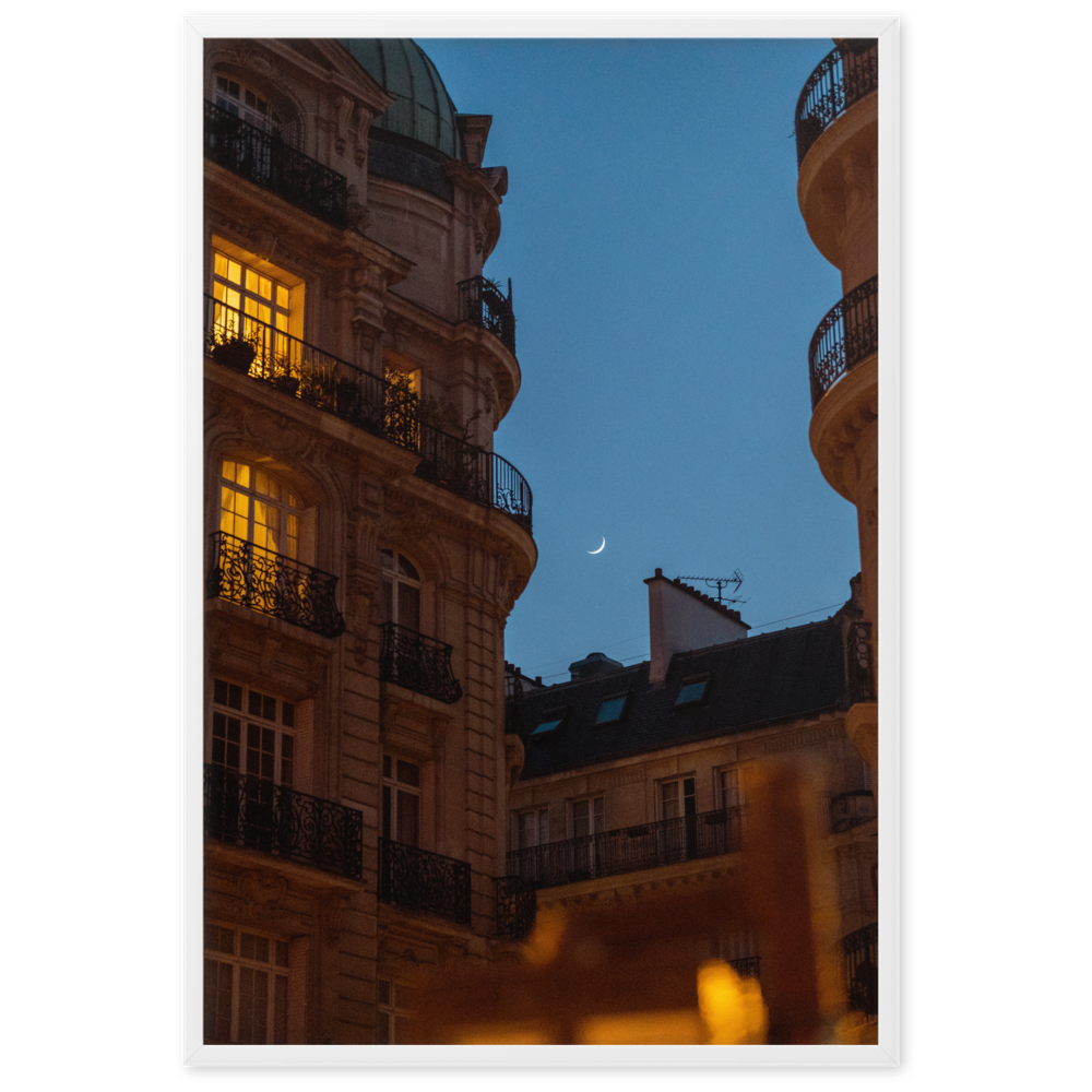 Croissant de lune entre des immeubles haussmanniens éclairés la nuit.