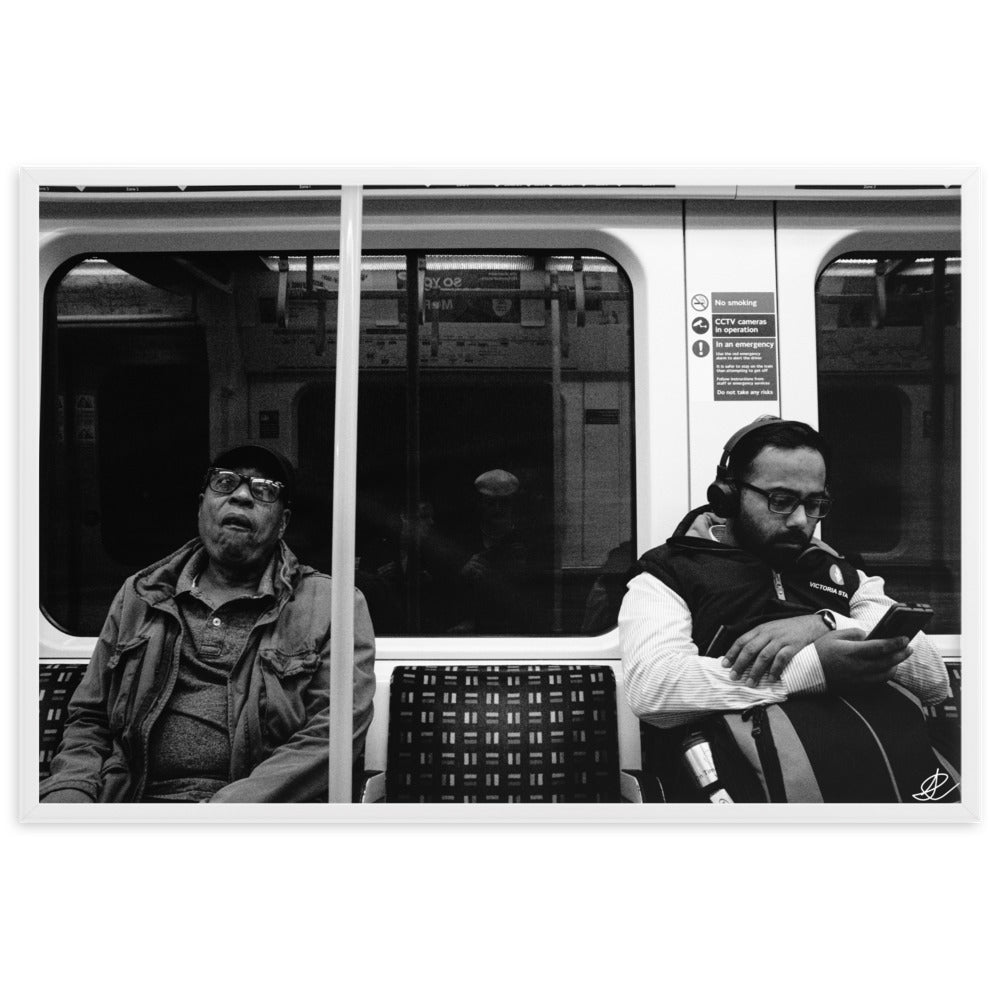 Poster encadré 'Fin de journée' en noir et blanc par Ilan Shoham, capturant une scène paisible du métro londonien avec un siège vide encadré par deux individus assis, symbolisant les distances sociales dans l'agitation urbaine.