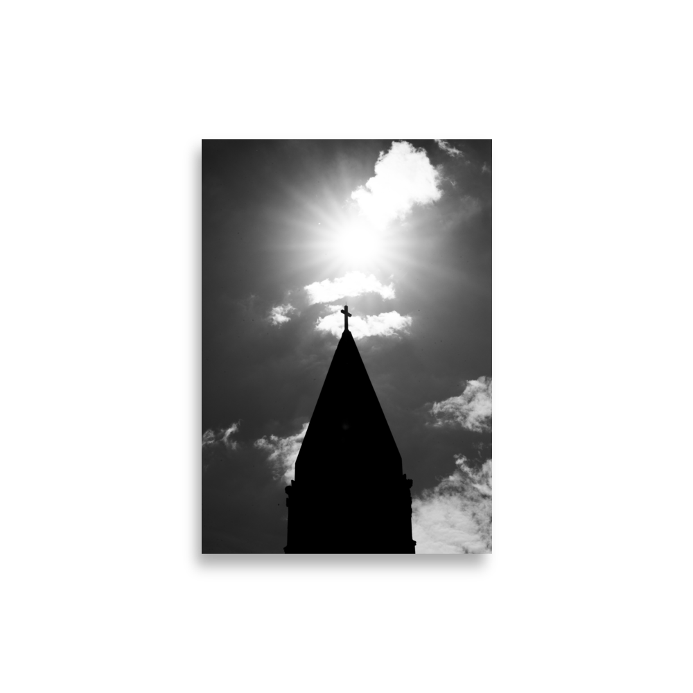 Photographie en noir et blanc du sommet d'une église avec une croix illuminée par le soleil.