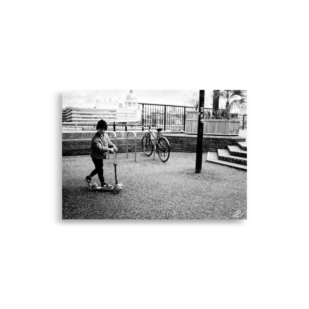 Photographie noir et blanc 'Trottinette' par Ilan Shoham, représentant un enfant joyeux trottinant sur les pavés de Londres, symbolisant l'innocence et la liberté