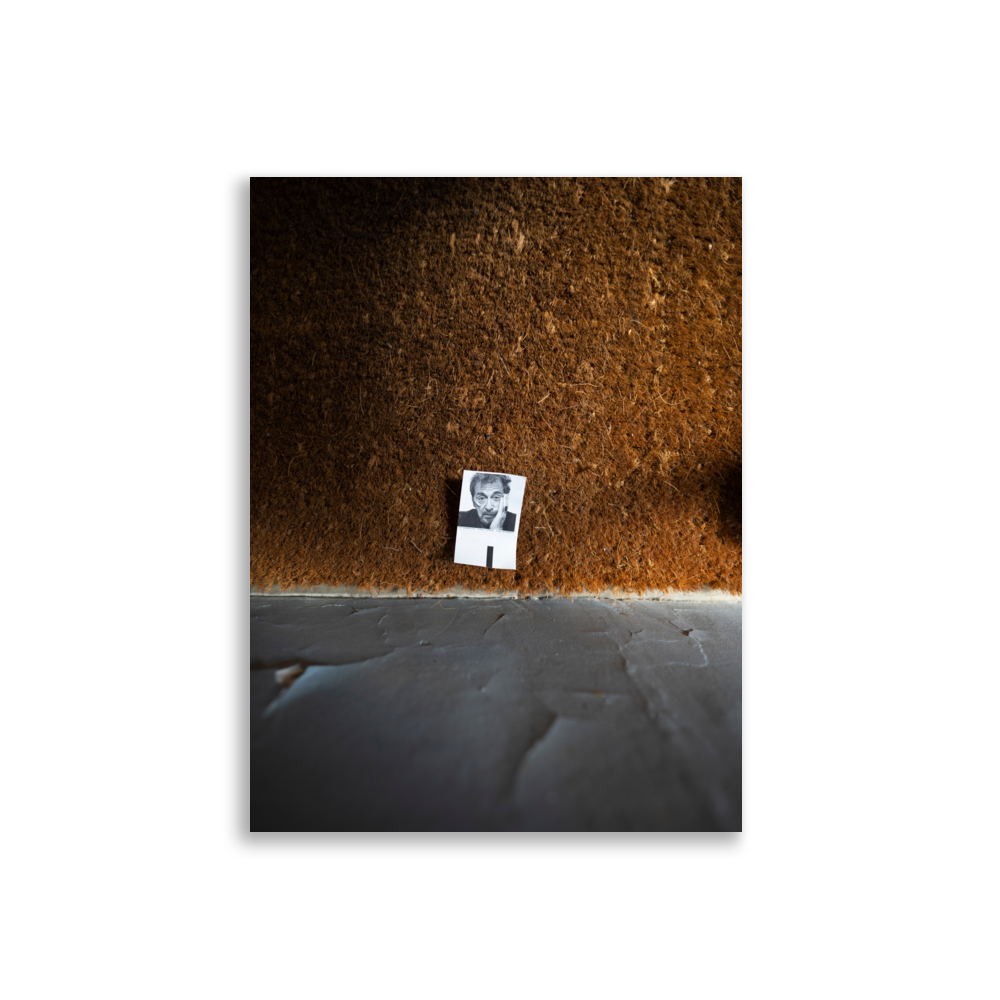 Poster d'une photographie représentant une petite photo posée sur un tapis à l'entrée d'un immeuble parisien.