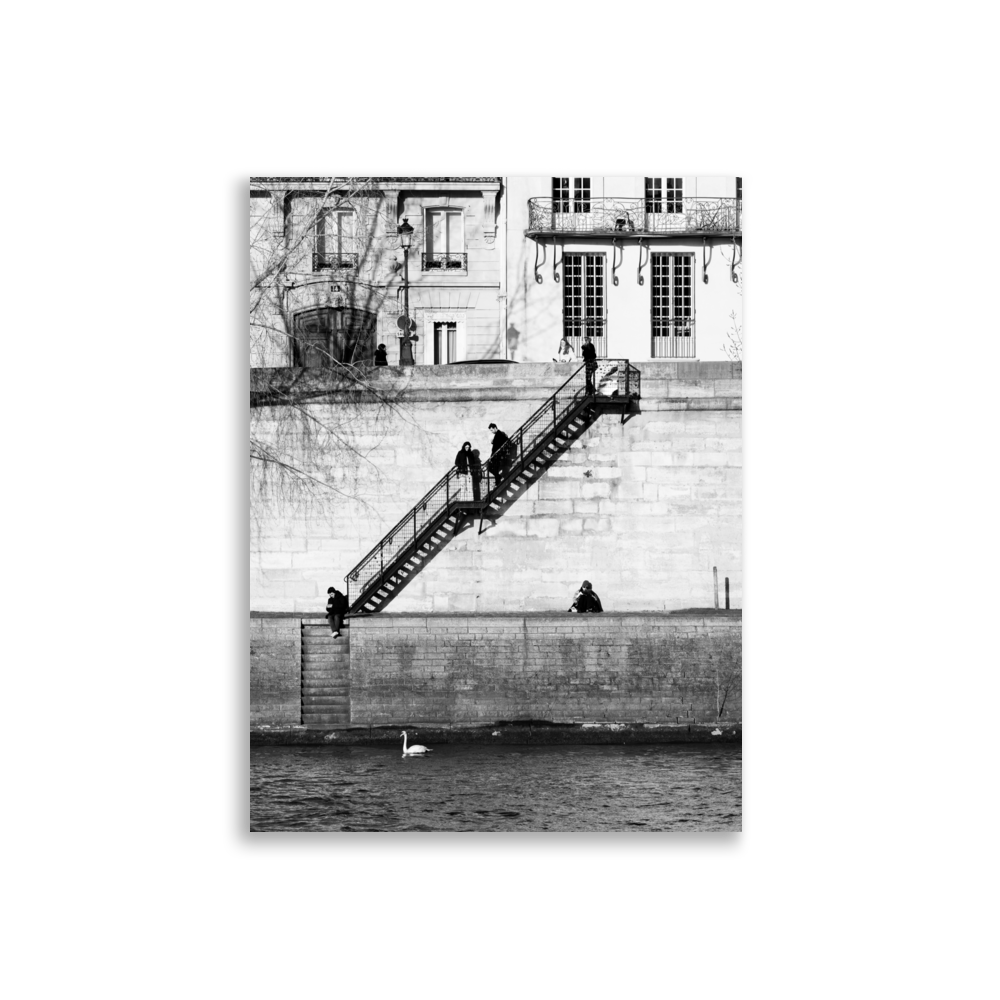 Photographie noir et blanc de personnes installées tranquillement sur les quais à Paris, encadrées par deux escaliers symétriques.