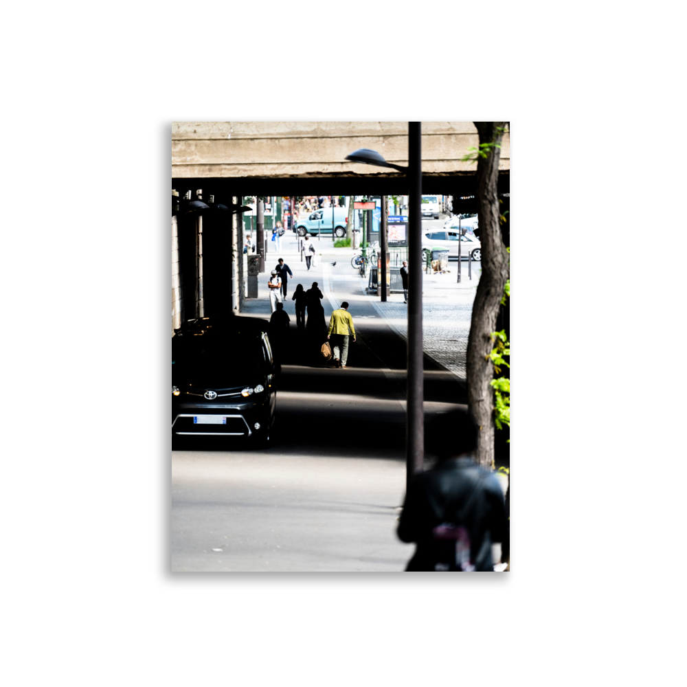 Un homme en veste verte kaki sous un pont ensoleillé.