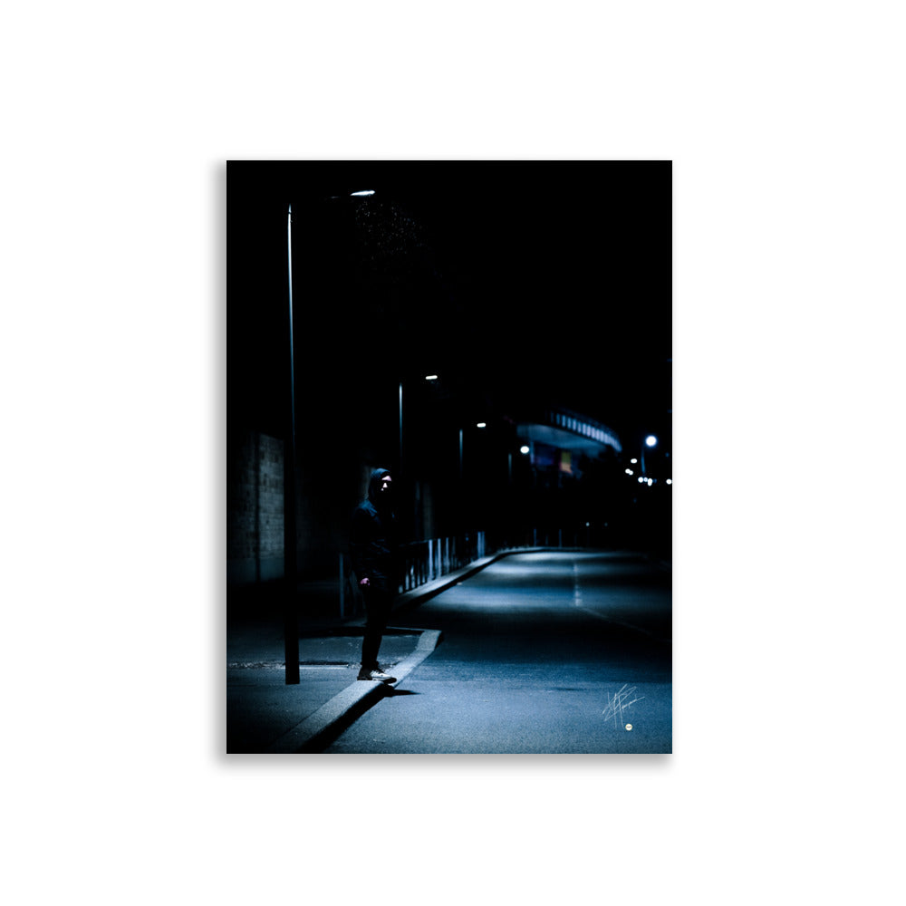 Photographie nocturne d'un homme à capuche se tenant sous un lampadaire près d'une station de métro à Créteil, émanant une atmosphère sombre et énigmatique.