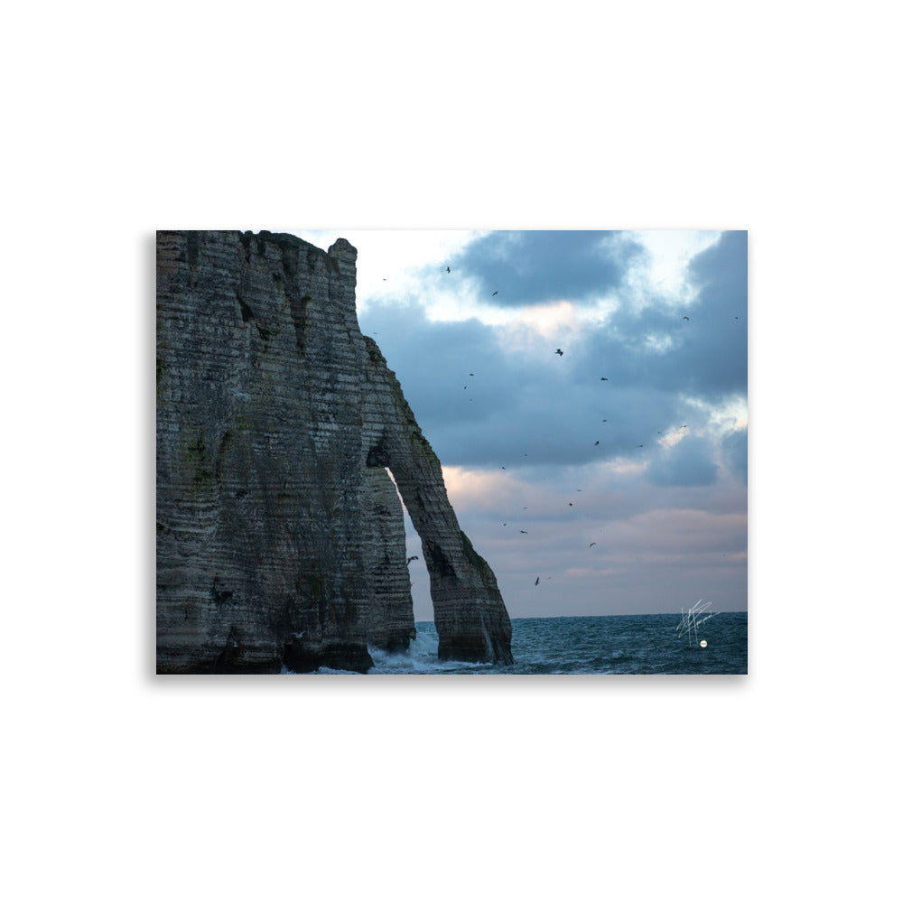 Vue panoramique des falaises d'Étretat avec des vagues s'écrasant puissamment sur la côte, sous un ciel nuageux où les mouettes virevoltent, incarnant la beauté sauvage de la Normandie.