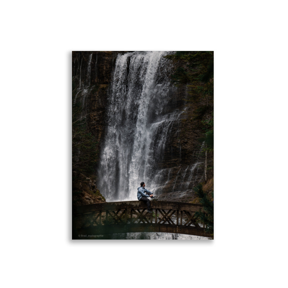 Homme méditatif assis sur une structure en bois au-dessus d'une rivière tumultueuse avec une cascade puissante en arrière-plan – photographie signée par Brad_explographie.