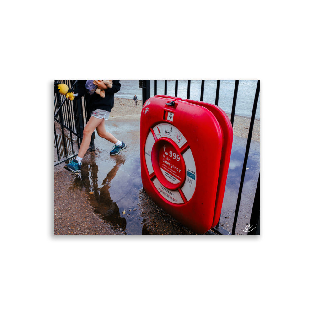 Photographie 'Il faut rentrer' par Ilan Shoham mettant en lumière une boite rouge d'urgence affichant le numéro 999, fixée sur une grille métallique, dans le contexte vibrant des rues de Londres.