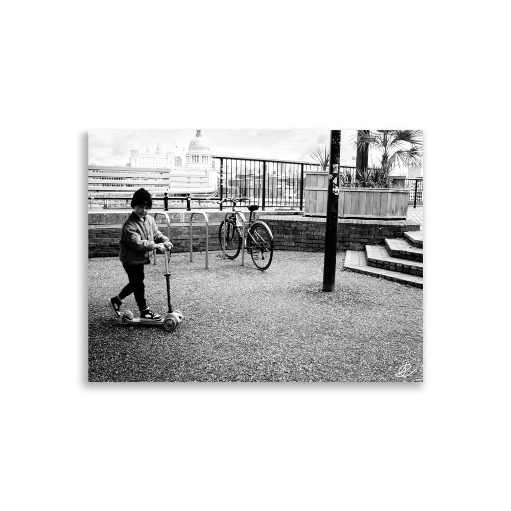 Photographie noir et blanc 'Trottinette' par Ilan Shoham, représentant un enfant joyeux trottinant sur les pavés de Londres, symbolisant l'innocence et la liberté