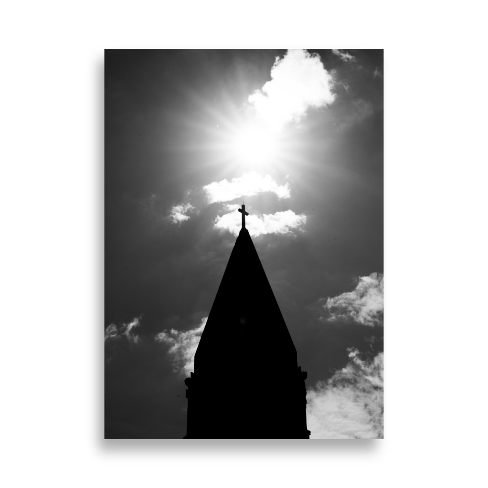 Photographie en noir et blanc du sommet d'une église avec une croix illuminée par le soleil.