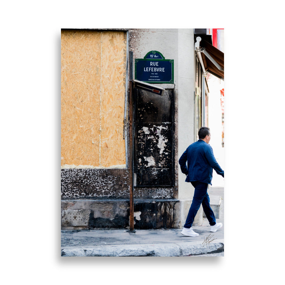 Photographie de la "Rue Lefebvre" après un incendie, montrant des traces de suie, un panneau de sens interdit plié et un passant.