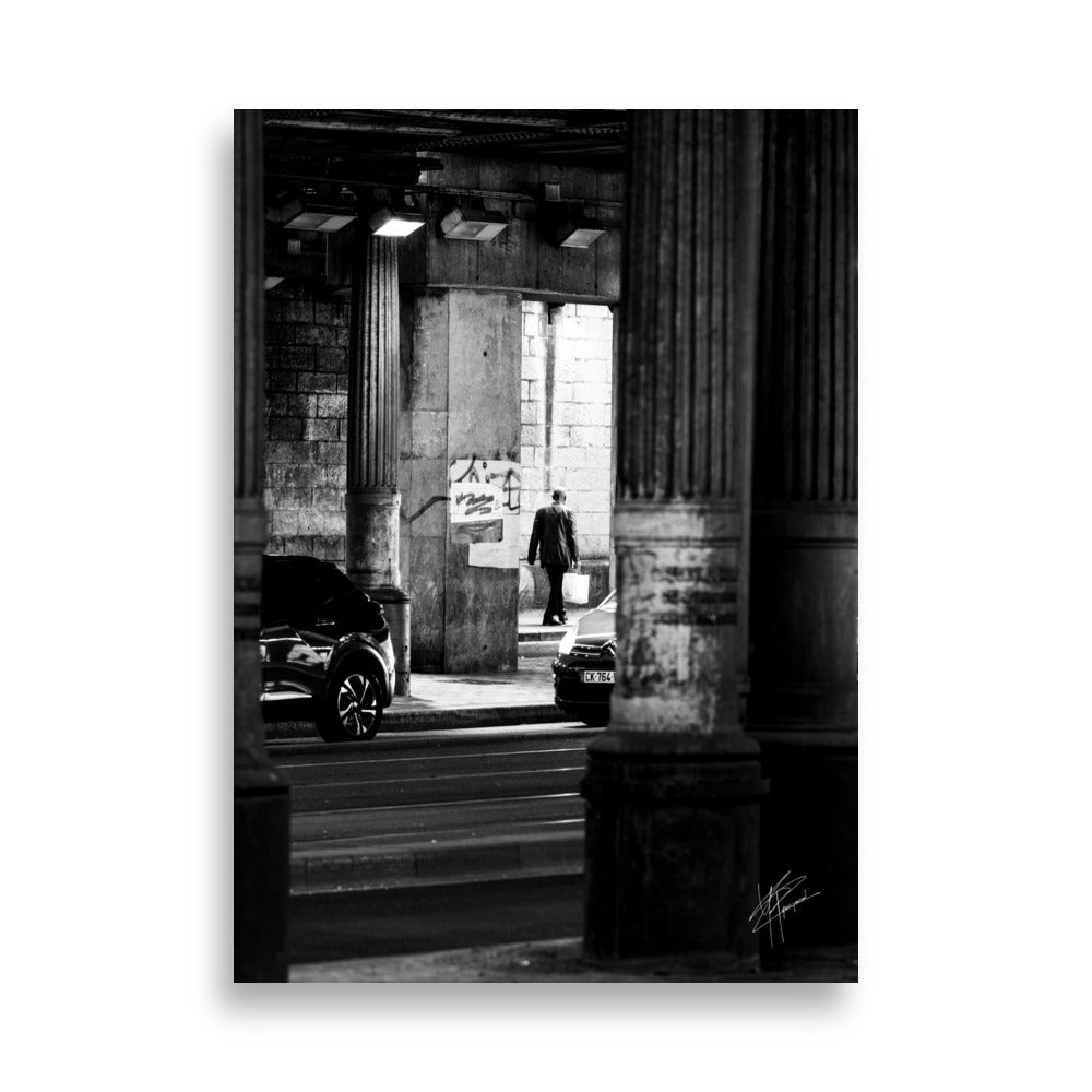 Photographie en noir et blanc, un homme sortant d'un tunnel sombre avec des sacs de courses, tandis que des voitures s'approchent de lui.