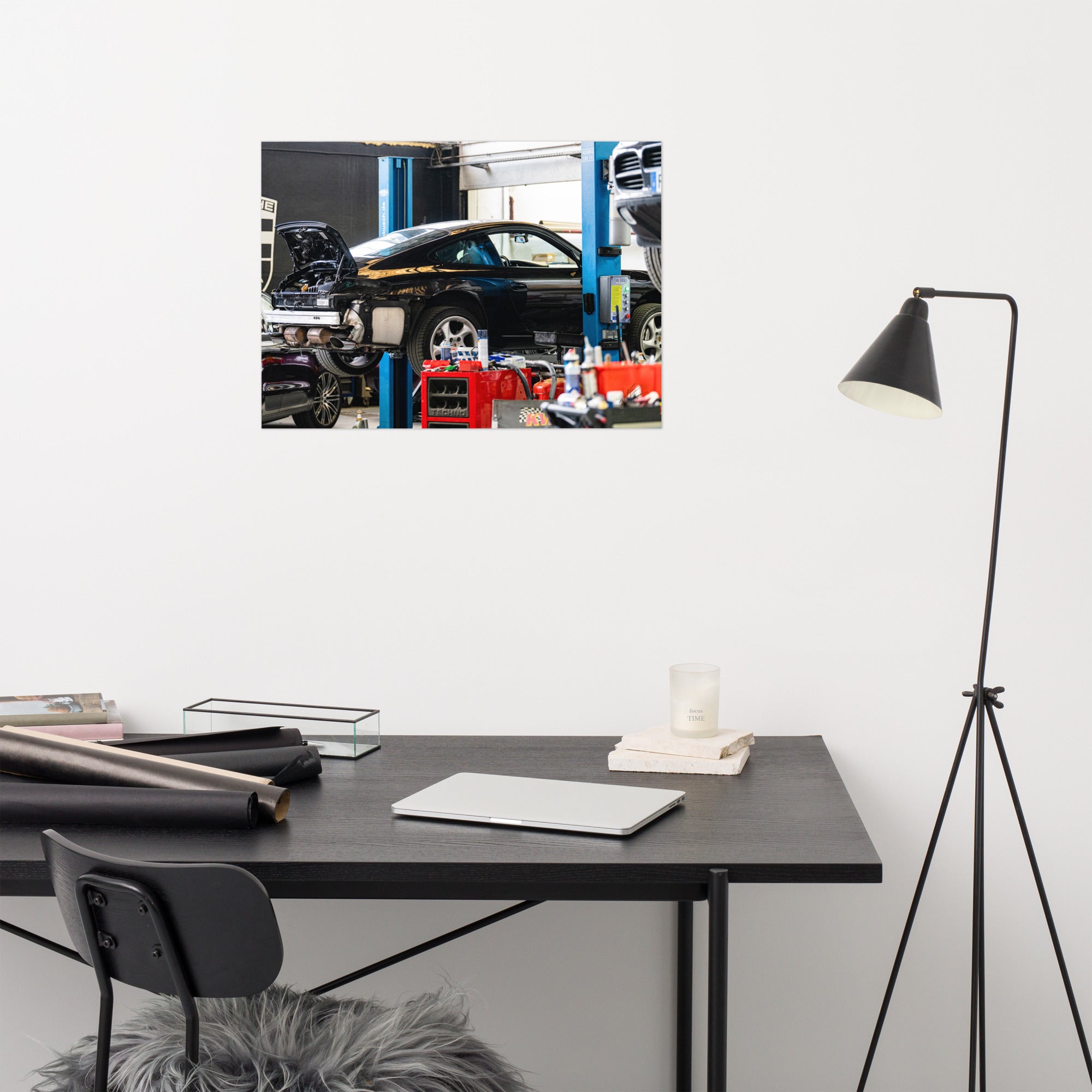 Photographie en noir et blanc d'une Porsche 911 sur un pont de révision, flanquée d'un Porsche Cayenne et d'un Porsche Macan dans un garage.