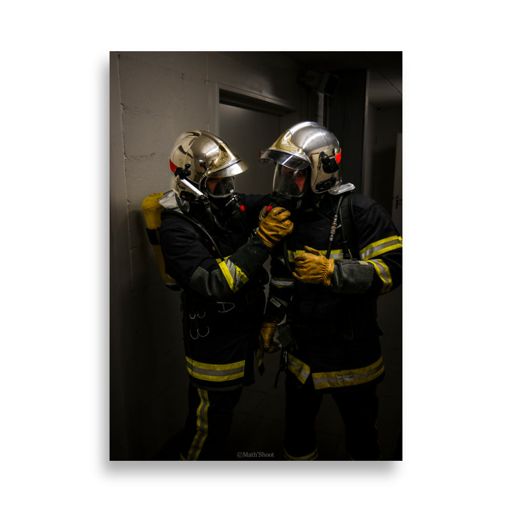 Photographie de deux pompiers en action, s'entraidant lors d'une intervention.