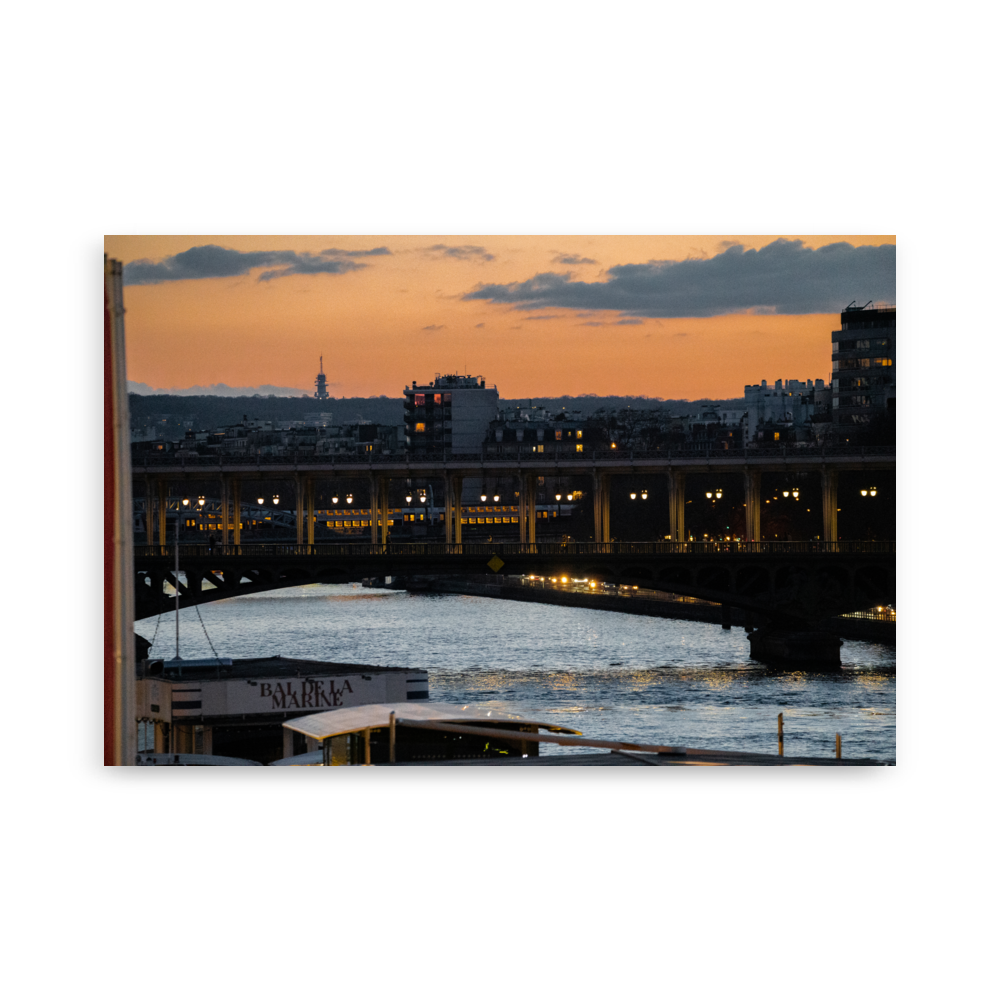 Photographie nocturne du Pont de Bir-Hakeim à Paris, avec des bateaux amarrés aux quais de la Seine et le RER en arrière-plan, sous un ciel teinté d'orange.