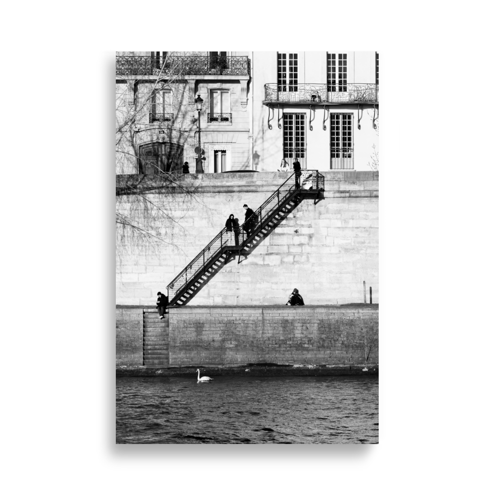 Photographie noir et blanc de personnes installées tranquillement sur les quais à Paris, encadrées par deux escaliers symétriques.