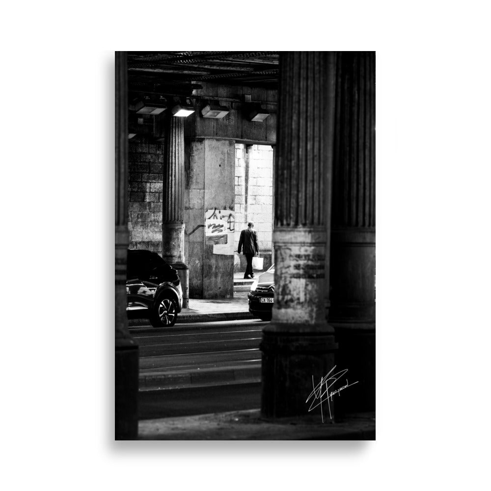 Photographie en noir et blanc, un homme sortant d'un tunnel sombre avec des sacs de courses, tandis que des voitures s'approchent de lui.