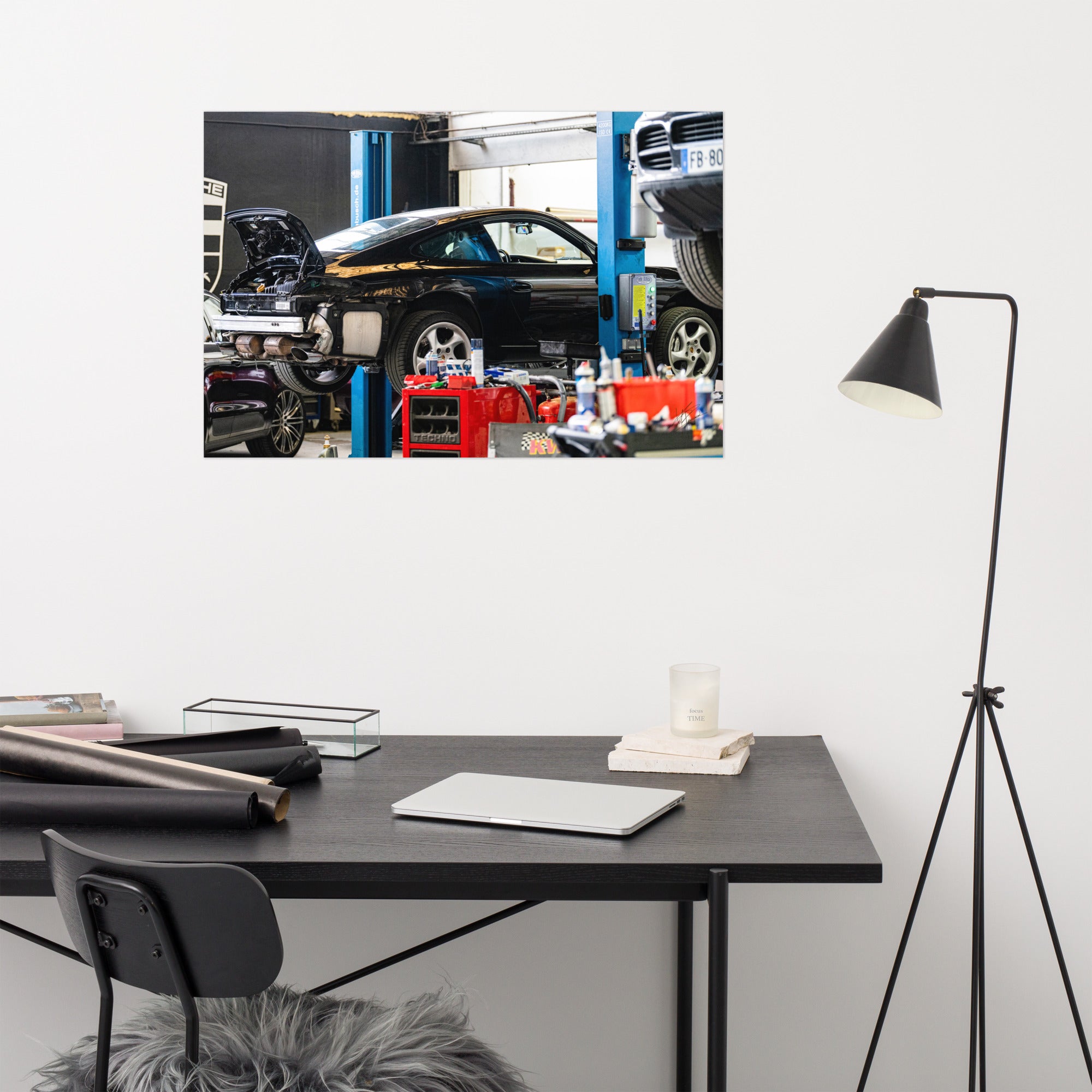 Photographie en noir et blanc d'une Porsche 911 sur un pont de révision, flanquée d'un Porsche Cayenne et d'un Porsche Macan dans un garage.