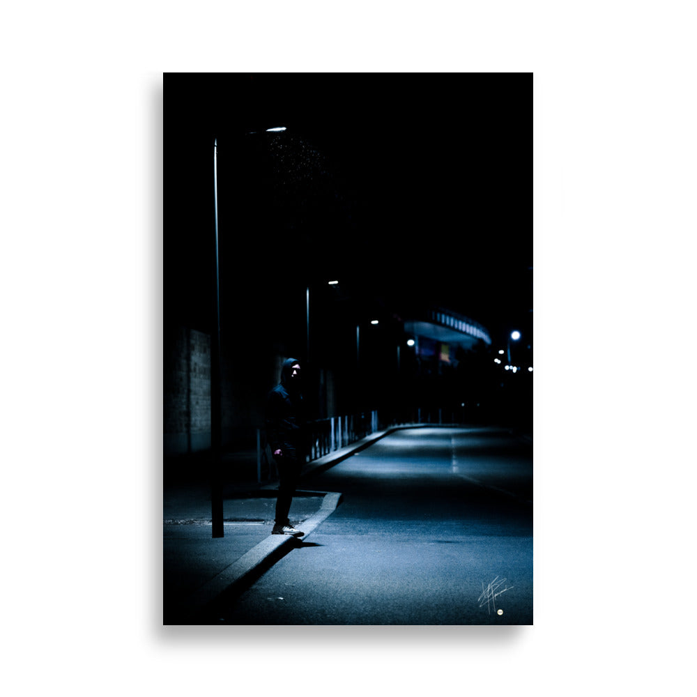 Photographie nocturne d'un homme à capuche se tenant sous un lampadaire près d'une station de métro à Créteil, émanant une atmosphère sombre et énigmatique.