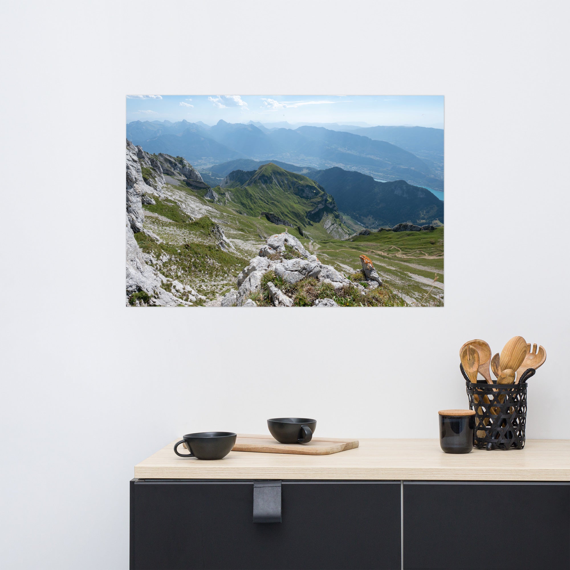 Vue panoramique du lac Annecy depuis les hauteurs, entouré de montagnes majestueuses avec un ciel serein au-dessus. Une représentation fidèle de la beauté naturelle des Alpes.