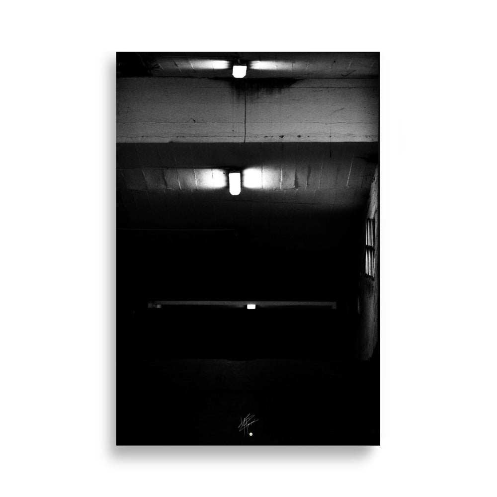 Photographie en noir et blanc intitulée 'Glaçant', montrant trois néons blancs éclairant une entrée de garage descendante dans une atmosphère sombre et mystérieuse.