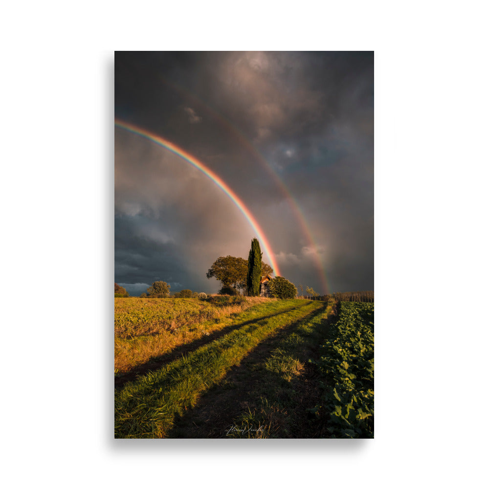 Photographie d'un paysage rural avec un double arc-en-ciel au-dessus d'une maison de campagne, capturée par Florian Vaucher, symbolisant un monde magique et plein d'espoir.