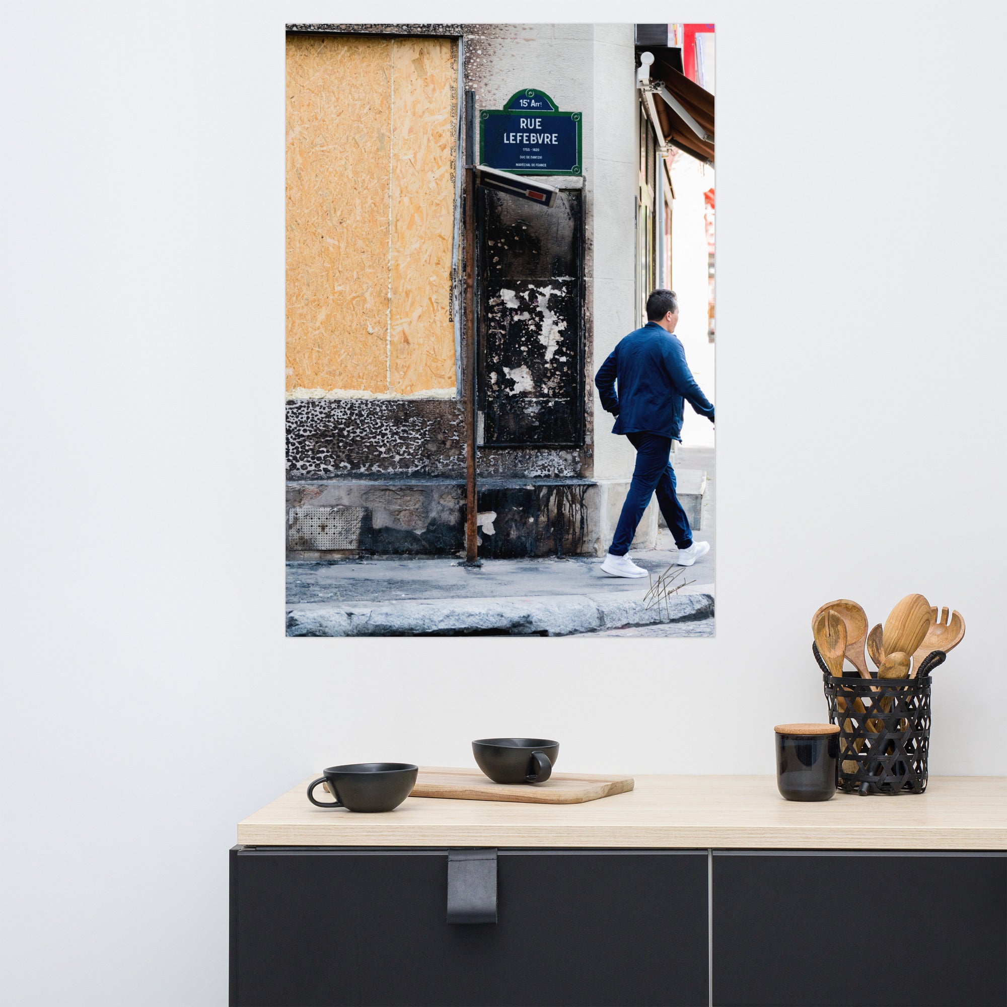 Photographie de la "Rue Lefebvre" après un incendie, montrant des traces de suie, un panneau de sens interdit plié et un passant.