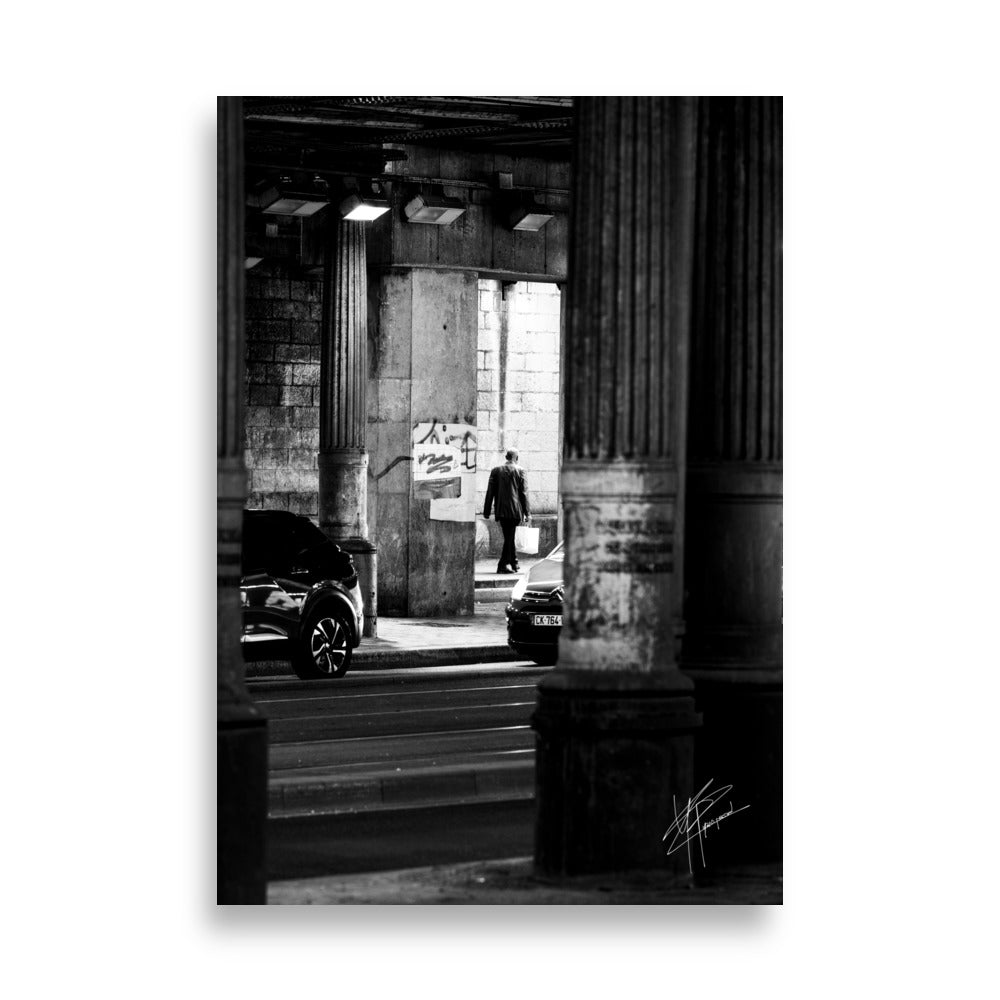 Photographie en noir et blanc, un homme sortant d'un tunnel sombre avec des sacs de courses, tandis que des voitures s'approchent de lui.