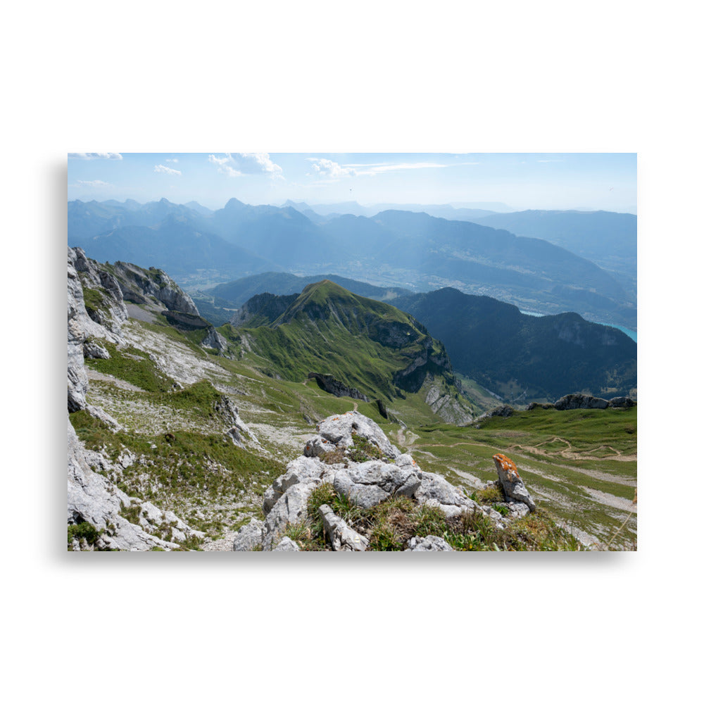 Vue panoramique du lac Annecy depuis les hauteurs, entouré de montagnes majestueuses avec un ciel serein au-dessus. Une représentation fidèle de la beauté naturelle des Alpes.