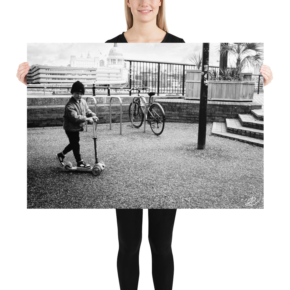 Photographie noir et blanc 'Trottinette' par Ilan Shoham, représentant un enfant joyeux trottinant sur les pavés de Londres, symbolisant l'innocence et la liberté